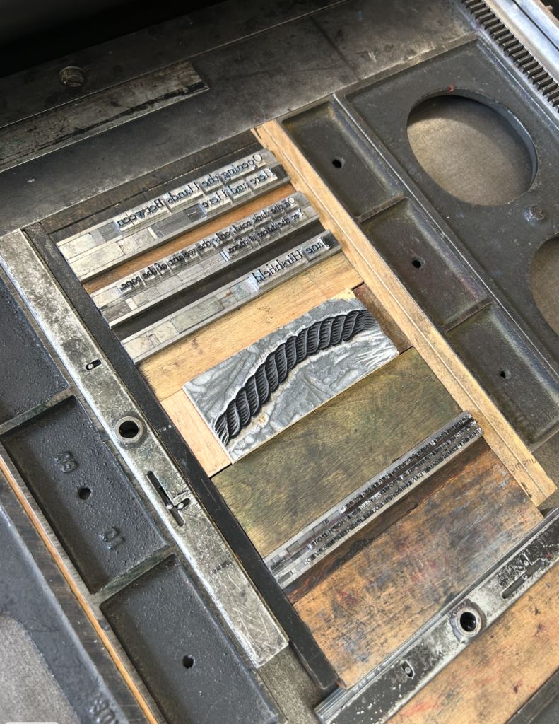 Metal setpieces rest in a metal printing press to be turned into prints.